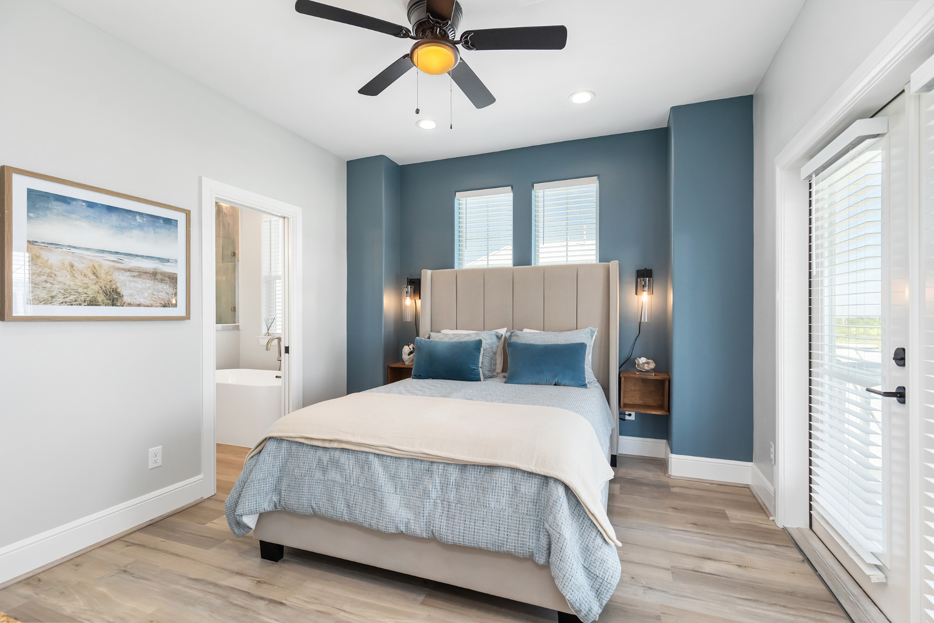 Primary bedroom with blue accent wall and beach artwork